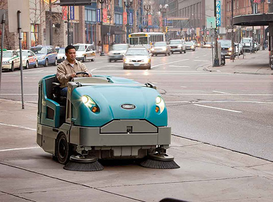 Varredeira S30 de tamanho médio com condutor limpando uma calçada da cidade.